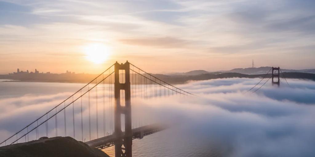Gün doğumunda alçak sisin içinden yükselen Golden Gate Köprüsü, soluk gökyüzüne karşı International Orange rengindeki kuleler