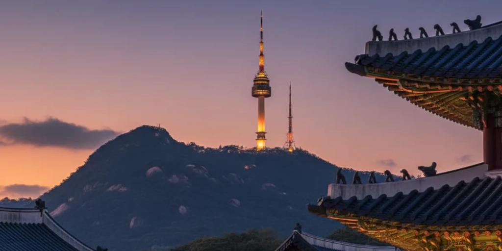 Ön planda Gyeongbokgung sarayının çatı çizgileri, arkada Namsan üzerinde yükselen N Seoul Tower