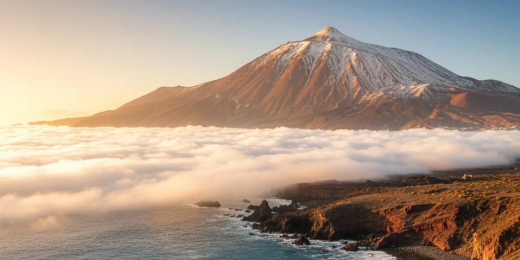 Bulutların ve Tenerife kıyı şeridinin üzerinde yükselen Teide Dağı