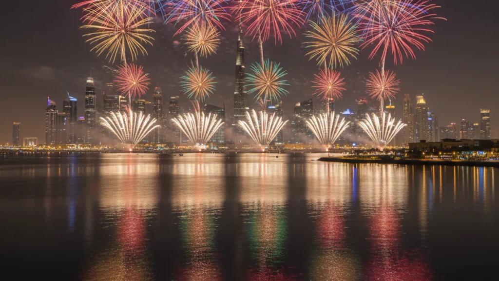 Dubai Alışveriş Festivali sırasında aydınlatılmış Dubai gökdelenlerinin ve kalabalık bir sahil yürüyüş yolunun üzerinde patlayan havai fişekler
