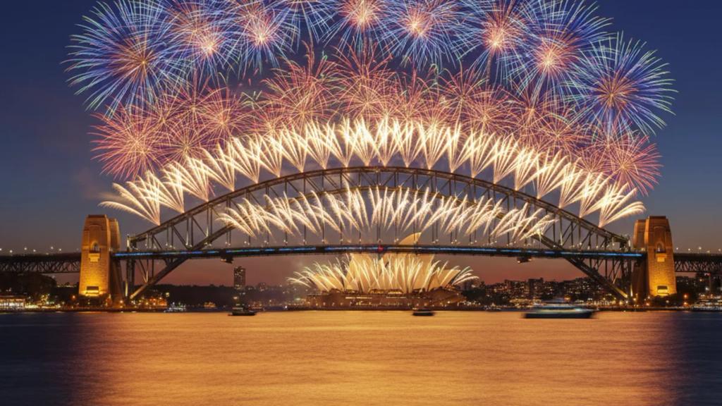 Yılbaşı gecesi gece yarısı Sydney Limanı Köprüsü ve Opera Binası üzerinde patlayan havai fişekler, kalabalık sahilden görünüm